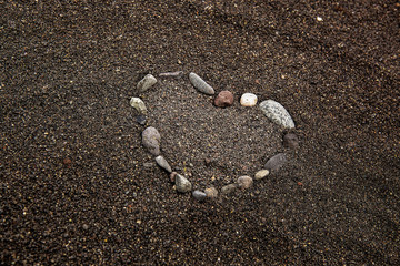 heart laid out of stones on the beach on black sand