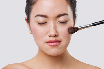 Close-up of young woman applying blush over white background