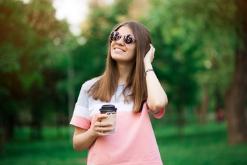 Coffee on go. Beautiful young woman in sunglasses holding coffee cup and smiling