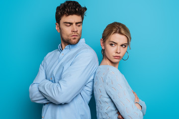 offended man and woman standing back to back with crossed arms on blue background
