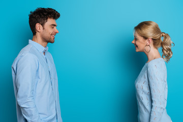 side view of happy man and woman smiling at each other on blue background