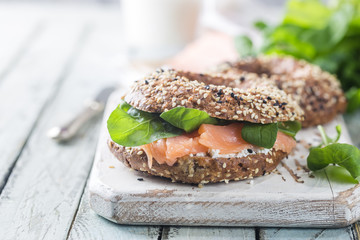 Bagels with cream cheese avocado, fish, arugula and radish on old wooden table. Healthy breakfast...