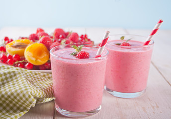 Rwo glass of raspberry smothies with berries on the plate on the white wooden table