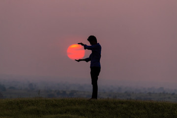 Silhouette of a man holding sun in his hands during the sunset