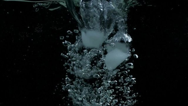 Slow motion ice cubes falling down in water on black background with splash, bubbles and drops