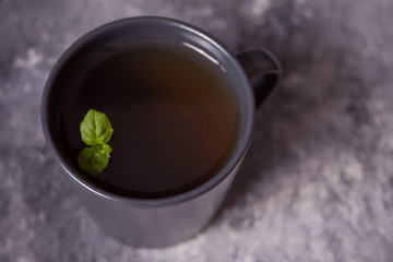 Gray mug of mint tea on dark stone background. Top view.