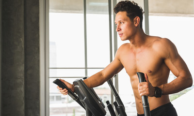 Obraz premium Young man at the gym exercising on the cross trainer machine. Fitness man doing cardio workout program.