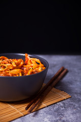 Udon noodles with chicken meat in bowl on dark stone background.
