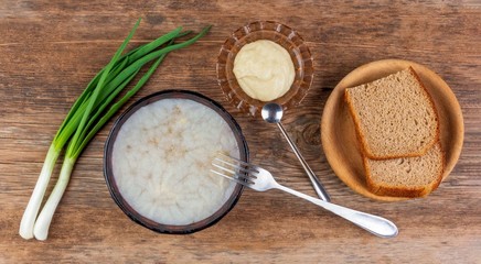 plate with jelly from aspic meat of poultry, beef and pork with a layer of fat, seasoning from ground horseradish and green onions and slices of rye bread on a wooden table top view close-up