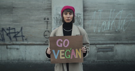 Young girl with Go vegan sign standing at empty street and looking to camera. Female hipster...