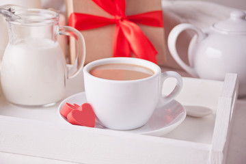 Obraz na płótnie Canvas Cup of coffee and a heart shaped red chocolate candies with gift box on the white tray