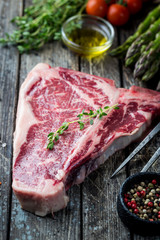 Raw T-bone Steak with fresh herbs and oil on dark wooden background