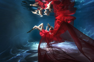 Underwater scene. A woman, a fashion model in the water in a beautiful dress swims like a fish. - obrazy, fototapety, plakaty
