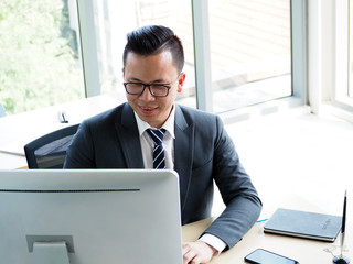  young asian businessman sitting in office and working with desktop computer.