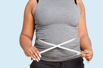 Mid section of woman measuring waist over blue background