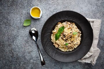 Risotto with mushrooms in a black plate over gray background, top view