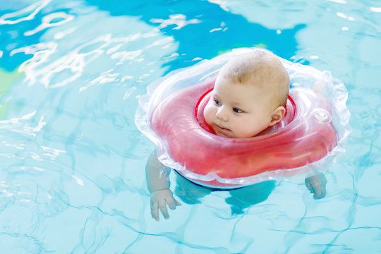 Cute little baby child learning to swim with swimming ring in an indoor pool. newborn girl or boy having fun in water. Active healthy leisure and sports for babies and children.
