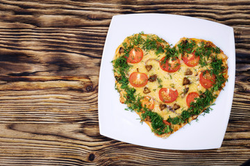 Valentines Day food. Heart shaped pizza with greens, on a white plate, on a wooden dark background. Top view. Copy space