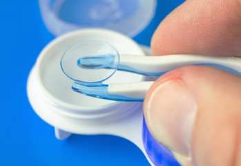 Hand with silicone tweezers takes out a soft contact lens  from the storage container. 