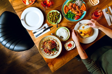 Woman dining in a Turkish restaurant with abundunt snacks on wooden table, top view