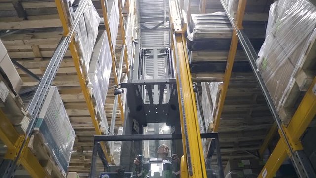 Warehouse male worker with forklift. loader unload goods from shelves. concept logistics, elevator, distribution. driver on car remove take down cargo cardboard box. delivering merchandise.