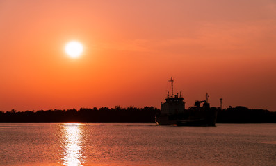 Obraz premium Dark shadow of larger fishing ship floating in the sea. With be hind background was silhouetted the mangrove forest along the coast. During in sunset and dark color the sky.