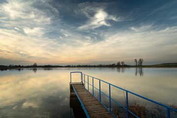 A bridge with a handrail on the lake, horizon and white clouds on a blue sky in Staw, Poland