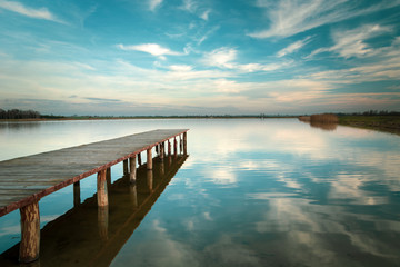 Long wooden bridge on the lake, horizon and white clouds on blue sky in Staw, Poland