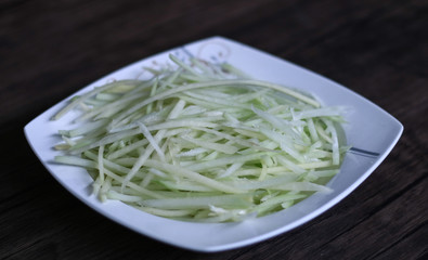 Shredded Green Papaya on white plate with wood background.