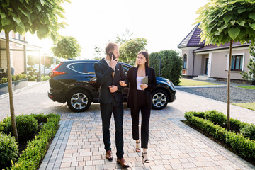 Full length of businessman and businesswoman walking outside office building on the business meeting, outdoors, on the background of the car and office center buildings. Business people meeting