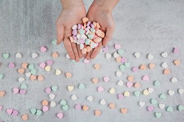 Valentine's Day  hands holding conversation heart candies and scattered conversation hearts  scattered on a gray cement neutral background