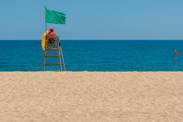 Lifeguard on rescue post at sand beach near sea with flag