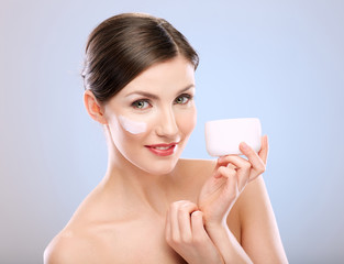 beautiful woman with cream on face holding white jar.