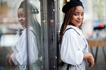 African american woman in overalls and beret posed in outdoor terrace with christmas decorations garland.