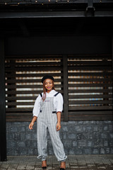 Fototapeta premium African american woman in overalls and beret posed outdoor against wooden background.