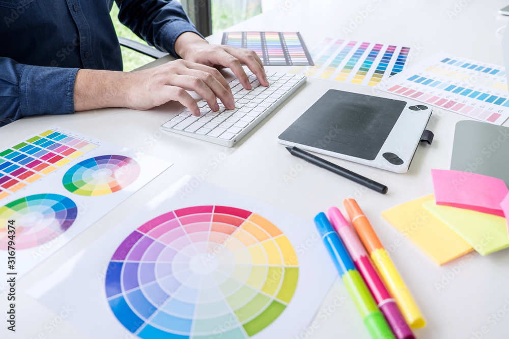 Poster Image of male creative graphic designer working on color selection and drawing on graphics tablet at workplace with work tools and accessories