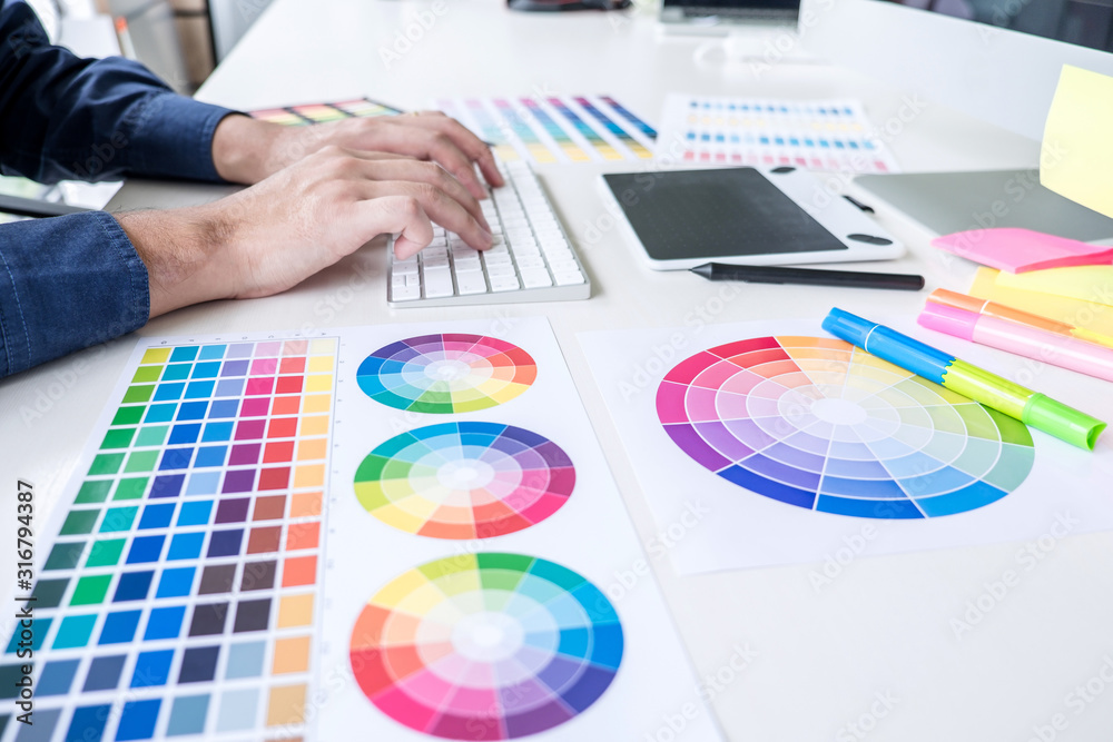 Poster Image of male creative graphic designer working on color selection and drawing on graphics tablet at workplace with work tools and accessories