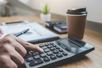 Businessman working on a graph document financial report and analysis calculation investment cost with calculator at office desk and other objects around