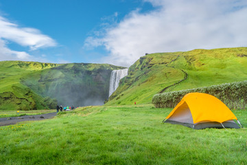 Camping site with tents in front of famous Skogarfoss waterfall, while hiking in Iceland, summer
