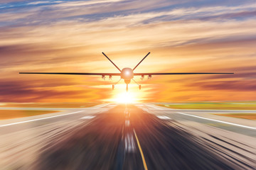 Military unmanned aerial vehicle takes off from runway at a military base in the evening at sunset.