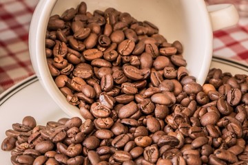 Roasted coffee beans in cup and plate on coffeeshop table. Fresh gourmet flavor aroma. Delicious fair trade cafe cappuccino or espresso ingredient. The bean bunch was fallen over at breakfast