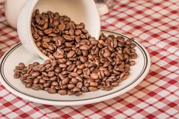 Roasted coffee beans in cup and plate on coffeeshop table. Fresh gourmet flavor aroma. Delicious fair trade cafe cappuccino or espresso ingredient. The bean bunch was fallen over at breakfast