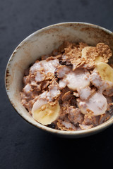 Bowl of granola with yogurt and banana. Concept for a tasty and healthy meal. Dark stone background. Close up.