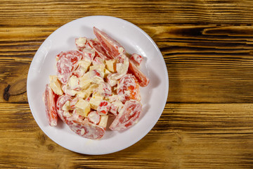 Tasty salad with crab sticks, cheese, tomato and mayonnaise on wooden table. Top view