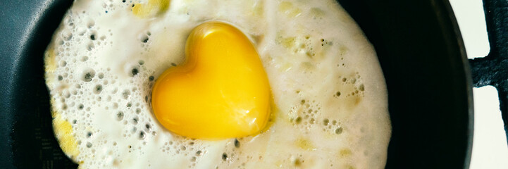 Banner of fried egg heart shaped in pan for Valentines Day. Morning cooking food background. Heart of symbol love. Stock photo.