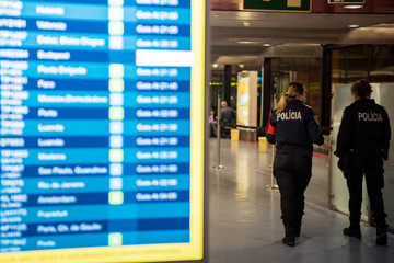 Couple of police women inside the Lisbon airport in Portugal. Information screen of flights in front.