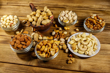 Assortment of nuts on wooden table. Almond, hazelnut, pistachio, peanut, walnut and cashew in small bowls. Healthy eating concept