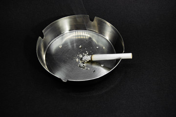 Smoking white cigarette on Ashtray with black background. Unhealthy smoking issues.