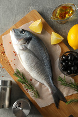 Cutting board with Dorado fish and cooking ingredients on grey background, top view