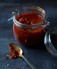 Closeup of wide mouth jar with homemade tomato perserves and tomato preserves on a spoon next to the jar